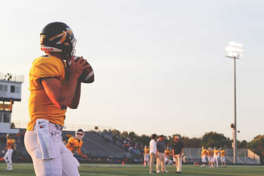 An American Football player in a yellow jersey holds the ball, preparing to throw it across the pitch.