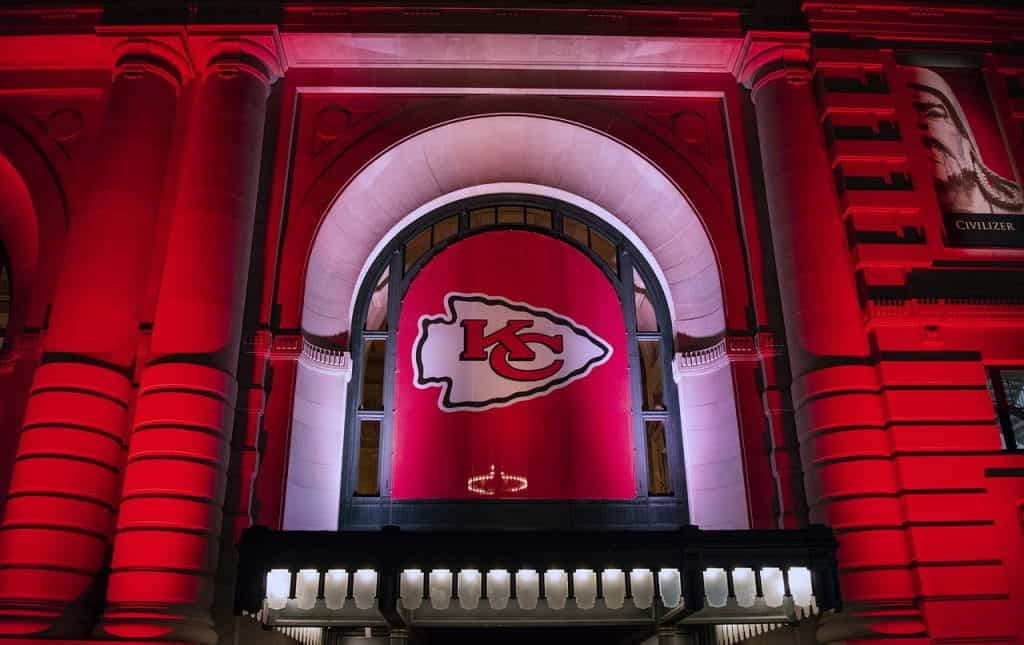 Building lit up in red lights with Kansas City Chiefs flag hanging from it