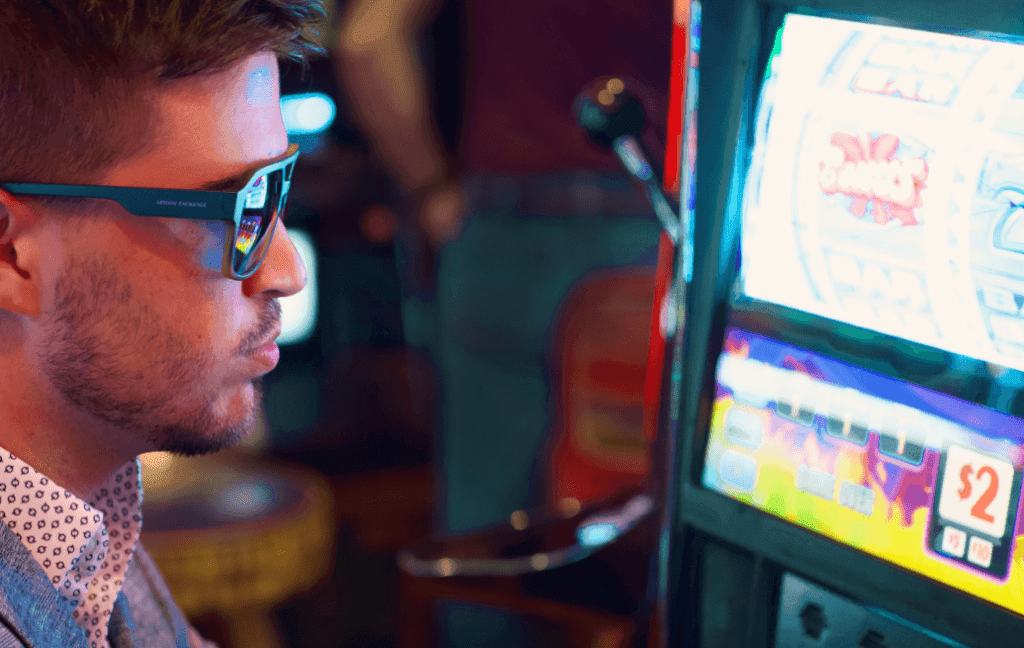 A man wearing sunglasses and a suit sits at a slot machine.