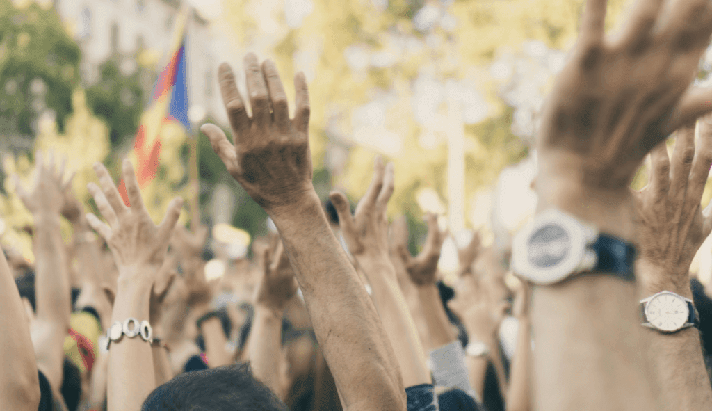 A color photograph of a crowd raising their arms in the air.