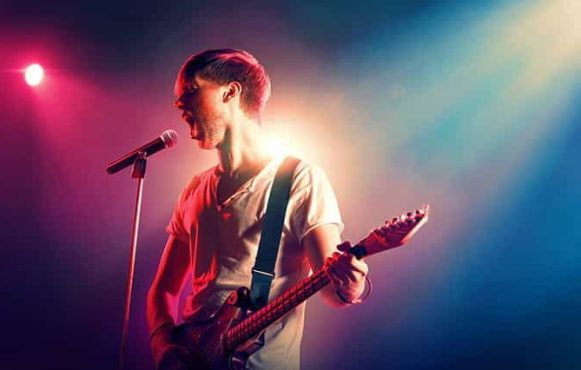 A man singing into a microphone while playing the guitar.