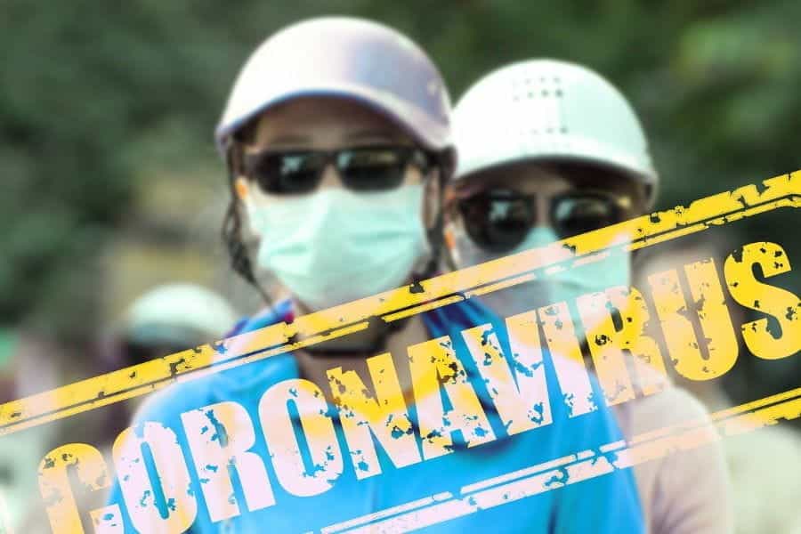 A yellow stamp reading CORONAVIRUS overlays an image of two people wearing baseball caps, sunglasses, and protective medical face masks.