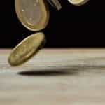 Euro coins fall onto a wooden tabletop.