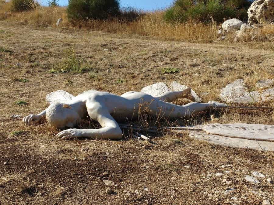 A statue of Icarus lies face-down on the ground.