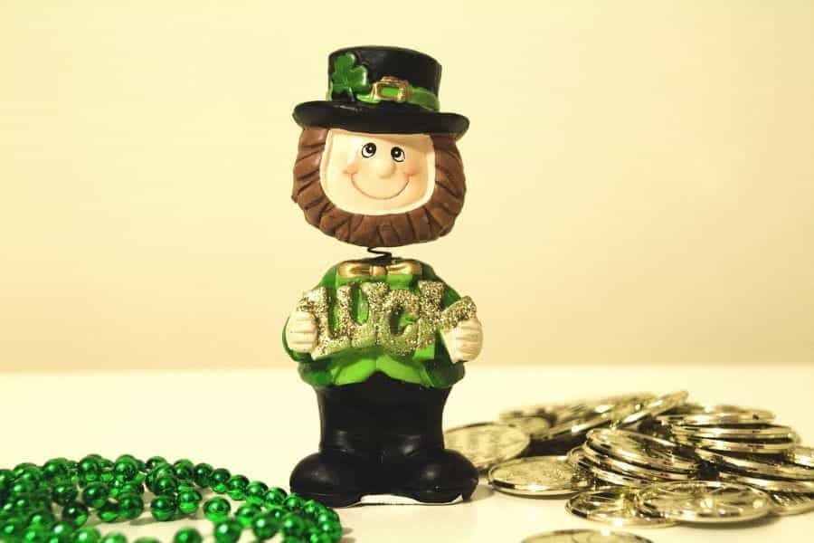 A leprechaun bobblehead, surrounded by green beads and gold coins, holds the word luck.