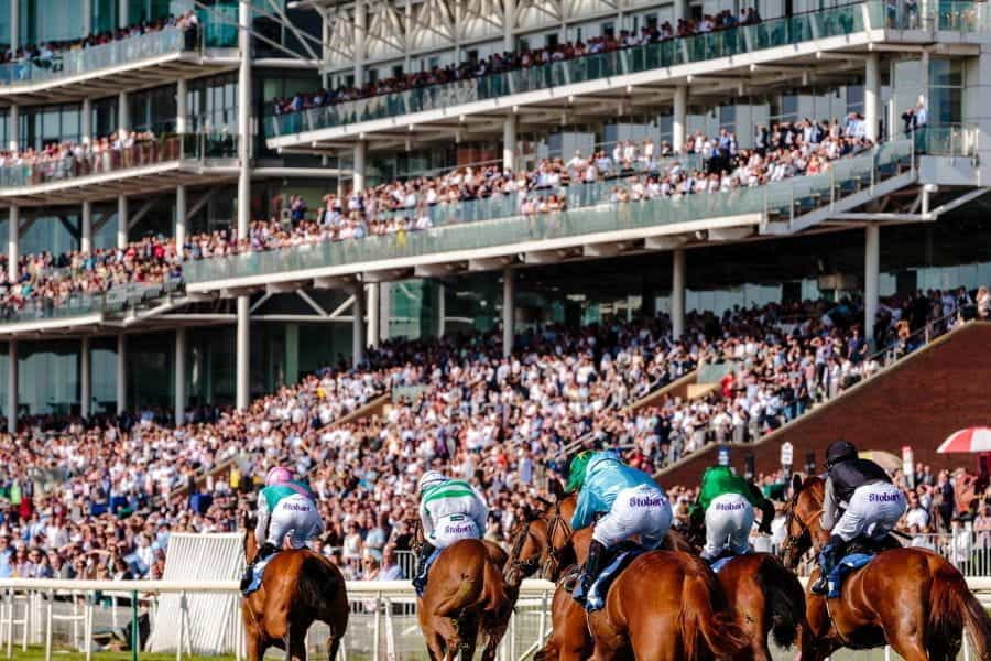 Horses race at a racetrack, with a crowd of spectators.