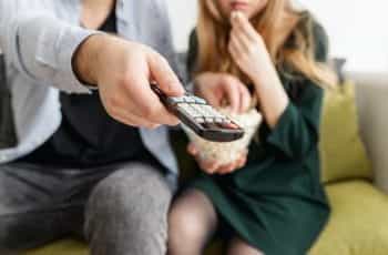 A man points a television remote, with popcorn and woman.