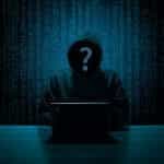 The silhouette of a faceless hacker stands before code.