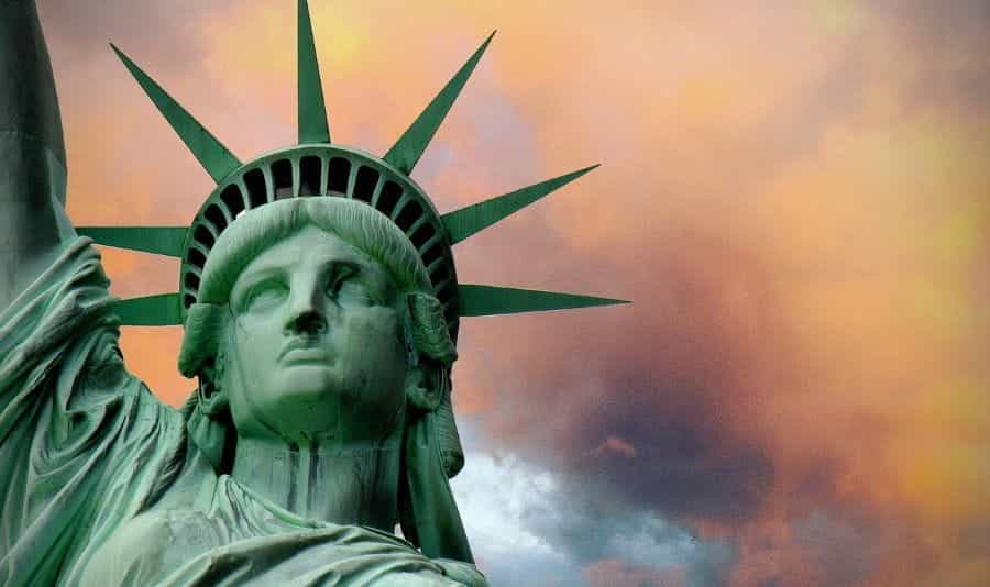 The Statue of Liberty in New York stands before pink sky.