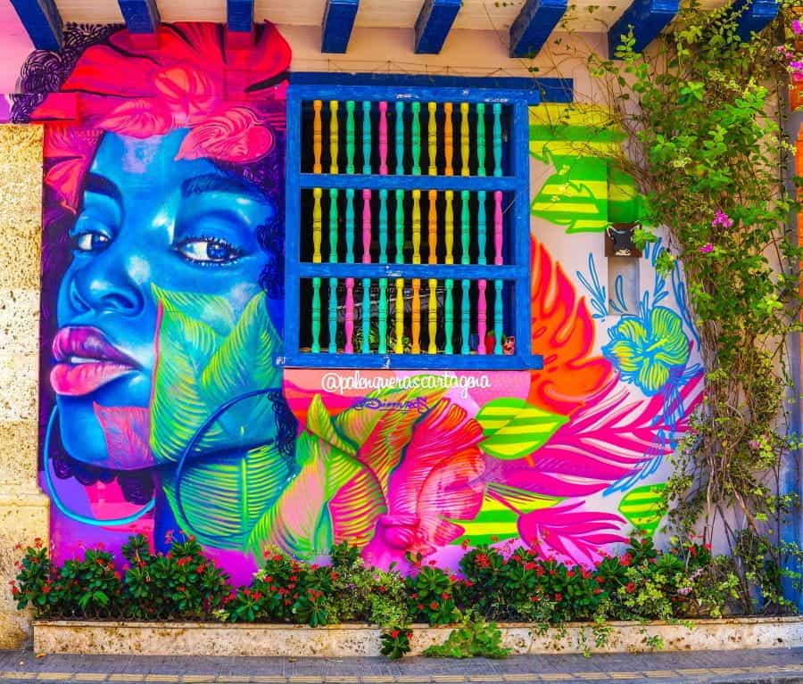 A colorful mural of a woman on a wall with barred windows in Cartagena, Colombia.
