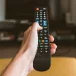 Hand holding a remote control pointed at a television.