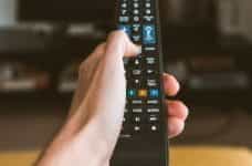 Hand holding a remote control pointed at a television.
