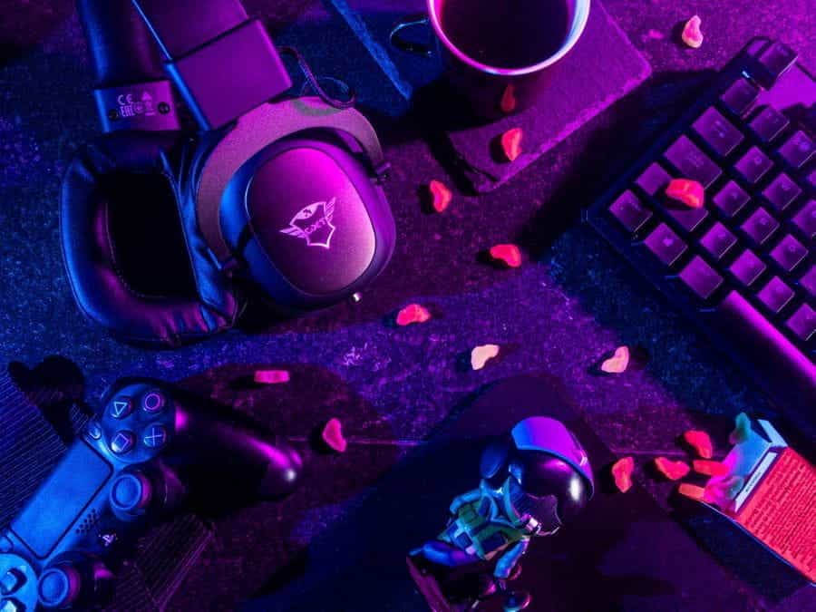Two gaming consoles and gaming headsets lie on a desk next to a keyboard.