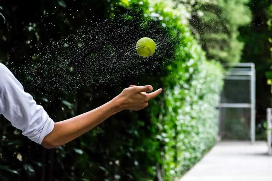A hand throws a green tennis ball, surrounded by water droplets.