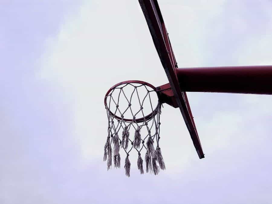A tattered basketball net hangs in front of gray sky.