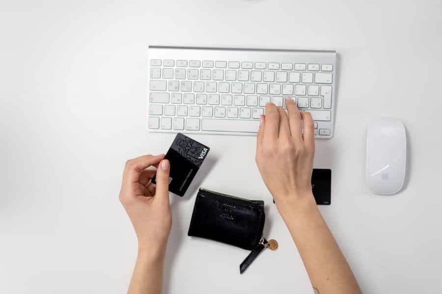 Someone typing on a computer keyboard, holding a credit card.