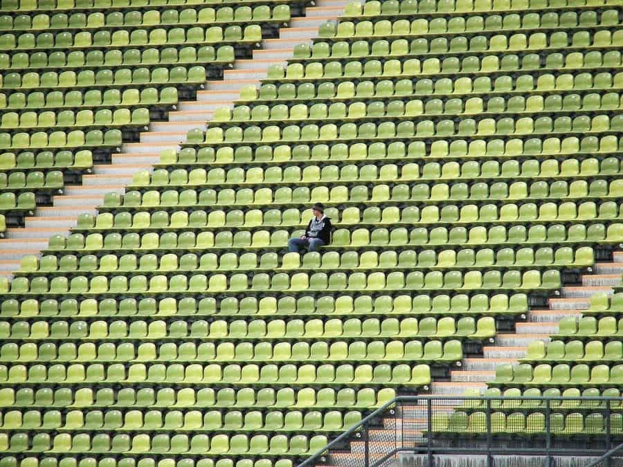 A single fan sitting in an empty football stadium.