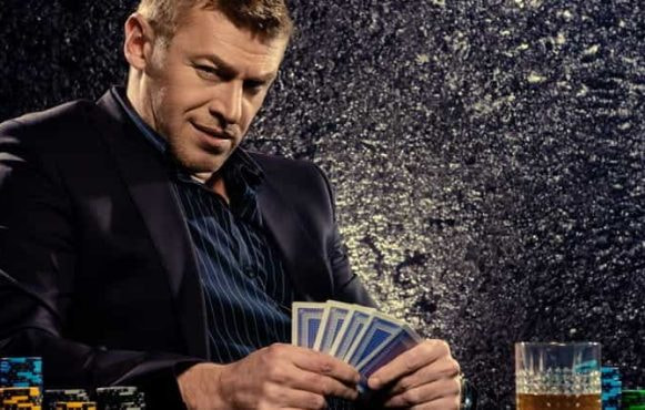 A man looking at the camera while holding a hand of cards.