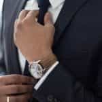 A businessman in a suit and expensive watch adjusts his tie.