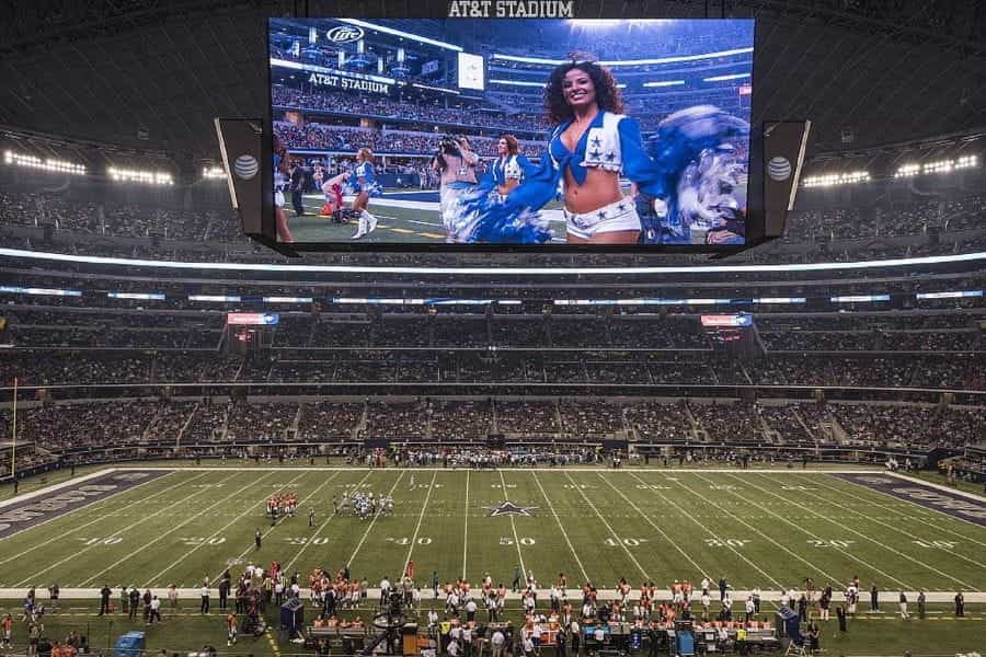 AT&T Stadium field before game with cheerleader on screen.