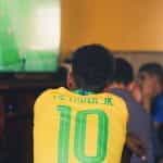 A boy in a Brazil soccer jersey watches soccer on TV at home.