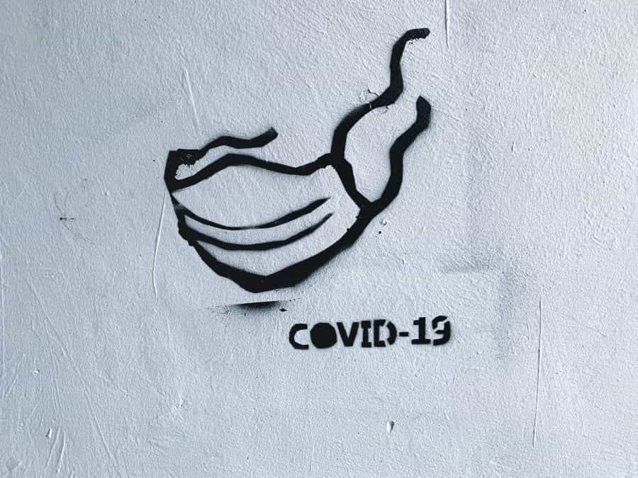 Graffiti of a mask and the words COVID-19 on a white wall.