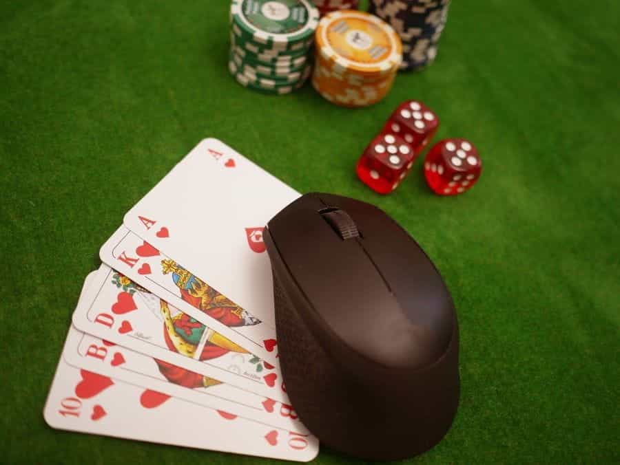 A computer mouse on a hand of cards next to some poker chips.
