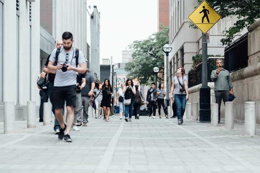 A group of tourists with cameras walk a city street.