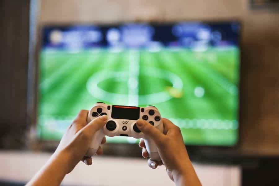 Person holds a gaming controller in front a football game.