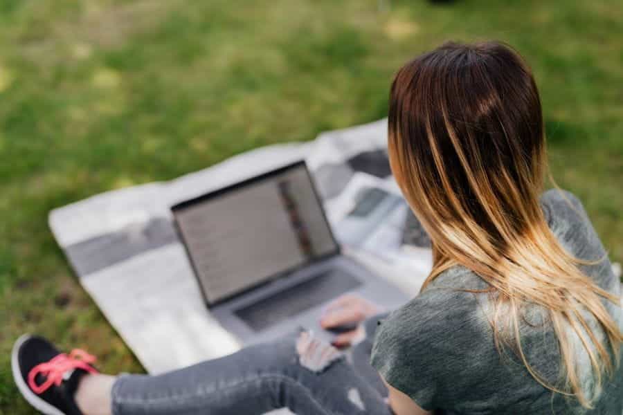 A teenage girl using a laptop in the park.