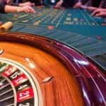 A roulette table in a casino with people around it.