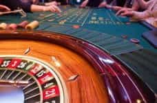 A roulette table in a casino with people around it.