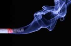 A lit cigarette smoking in front of a black background.