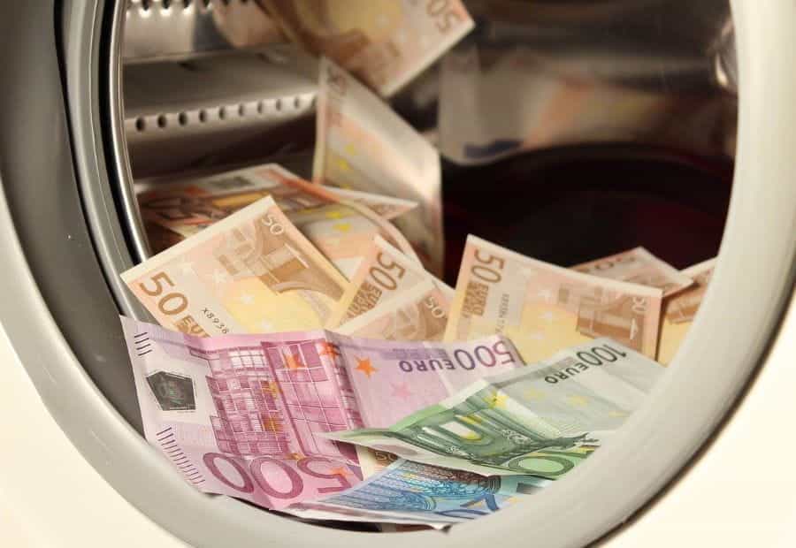 Many bank notes lie inside a washing machine, a pun for money laundering.