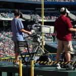 Two camera operators film a baseball game in an arena.
