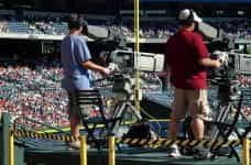 Two camera operators film a baseball game in an arena.