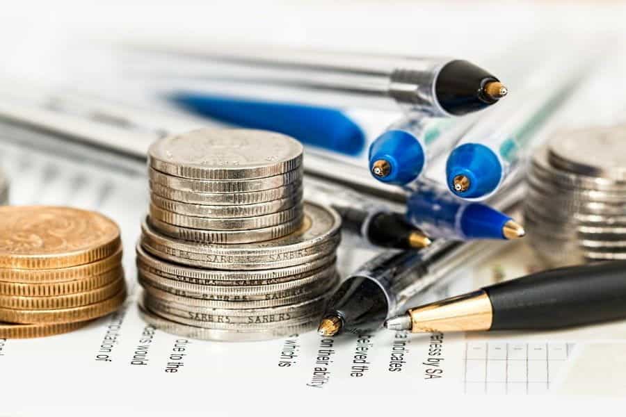 Piles of coins next to a pile of pens on top of a document.