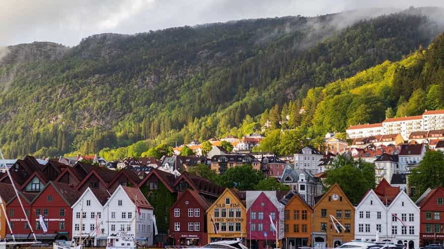 Colourful houses next to a port in Norway. A forested mountain is in the background.