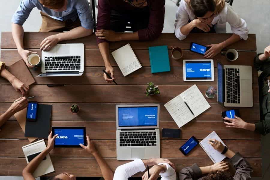 A team meeting around a wooden table, with laptops.
