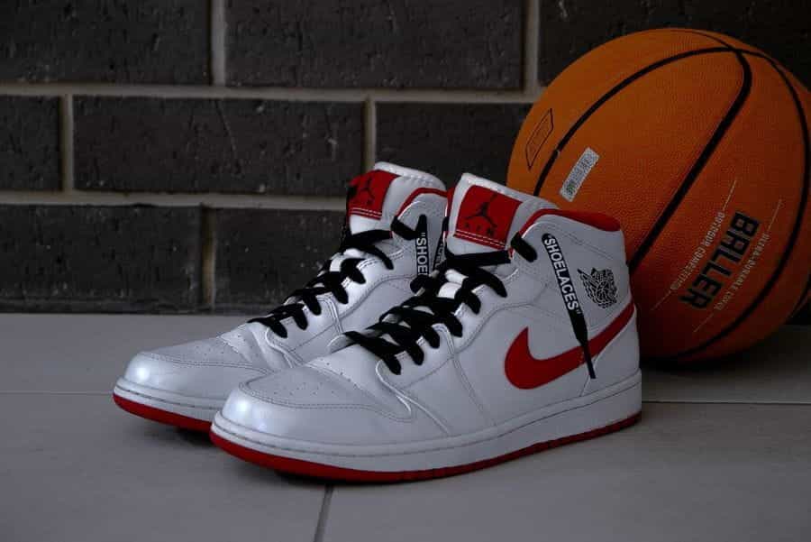 A white and red pair of Air Jordans lean against an orange basketball.