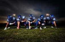 Five male American football players wearing blue uniforms prepare for their next play.