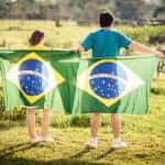 A man and a woman turn their backs to the camera and hold Brazilian flags behind them.