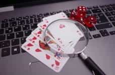 Several playing cards and a pair of dice lie on a computer keyboard under a magnifying glass.