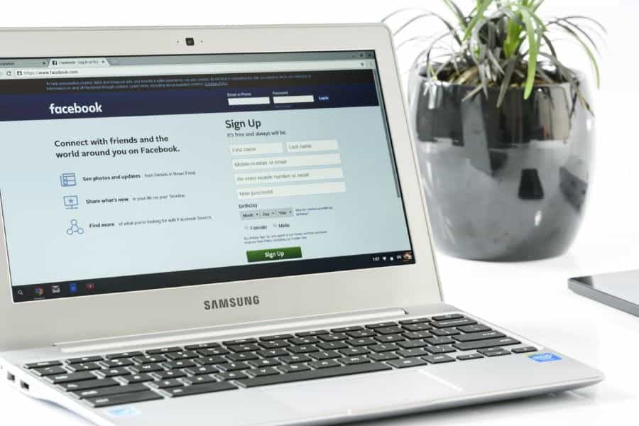 A laptop on a desk next to a plant, showing the Facebook website.
