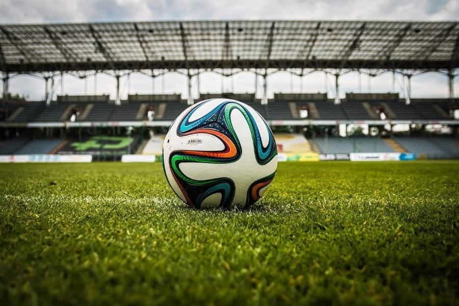 A football on the pitch with the stadium in the background.