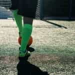 A footballer in green socks and boots, with foot on orange ball.