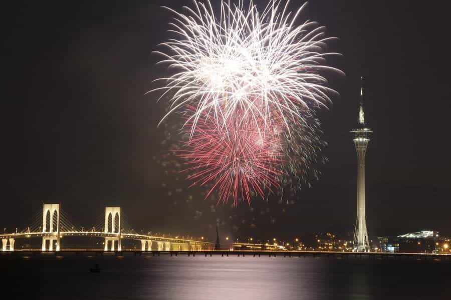 Fireworks going off over Macau at night with a tower and a bridge in the background.