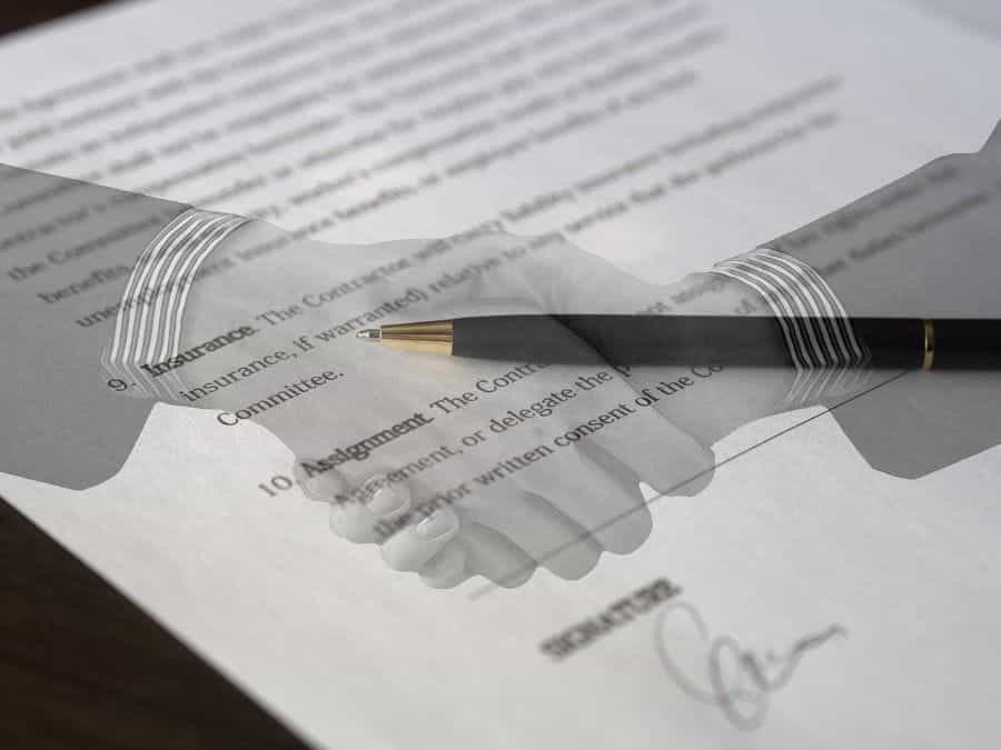 Two hands shake over a close-up view of a business contract.