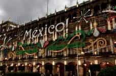A sparkly sign on an old building reads "MEXICO!" in white, green, and red.