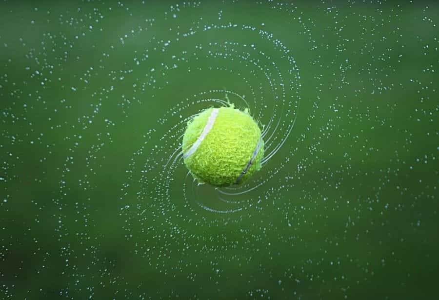 A wet tennis ball spinning and sending off droplets of water.